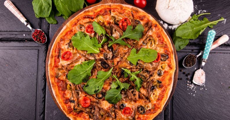 Spices And Herbs - A pizza with mushrooms, spinach and tomatoes on a black table