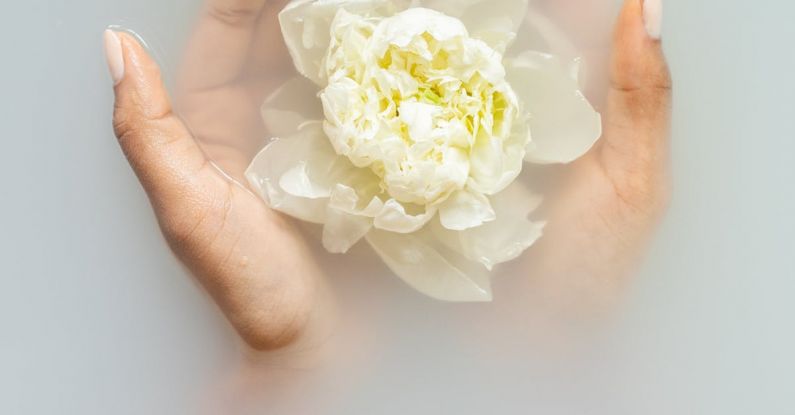 Organic Beauty - Unrecognizable female with soft manicured hands holding white flower with delicate petals in hands during spa procedures